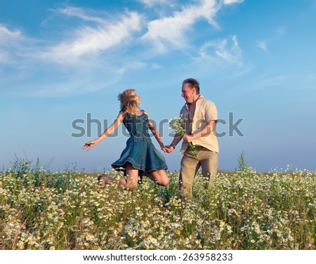 Happy man and the woman jump in the field with camomiles