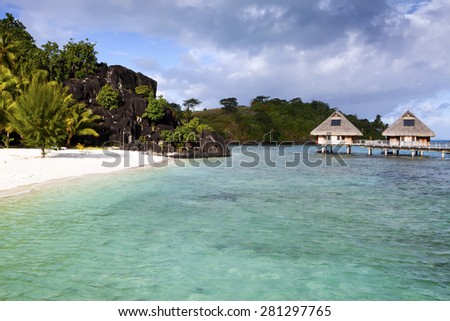 Typical Polynesian landscape - island with palm trees and small houses on water in the ocean and mountains on a background
