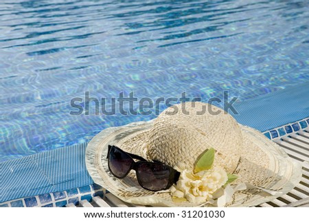 The straw hat and sun glasses lie on the brink of pool