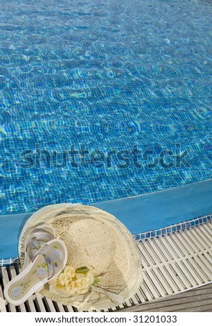 The straw hat and beach slippers lie on the brink of pool