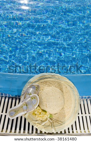 The straw hat and beach slippers lies on the brink of pool