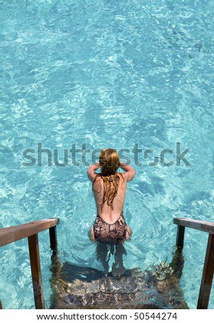 Maldives.  Young sports woman swims from steps of villa on water.