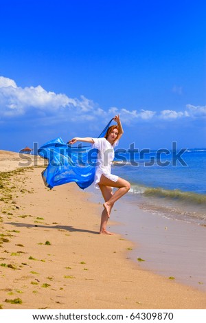 Young graceful woman  in white tunic with cape in hands  Dances on coast of ocean