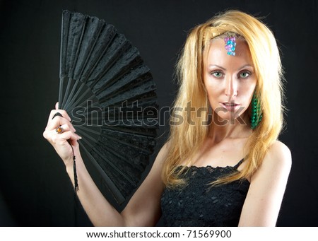 The beautiful young woman with long  blonde hair and  fan and jewellry on  dark background