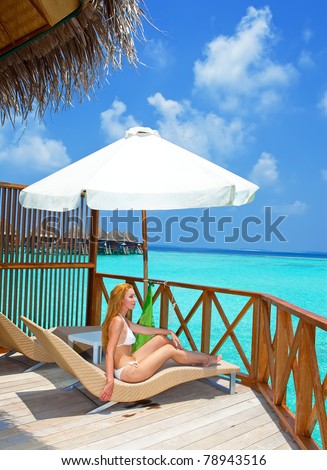The beautiful young woman on a terrace has a rest in a chaise lounge and looks at the sea