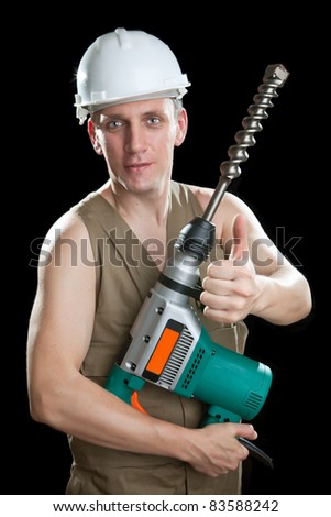 The builder in a protective helmet holds the professional puncher-hammer with a drill of the big diameter