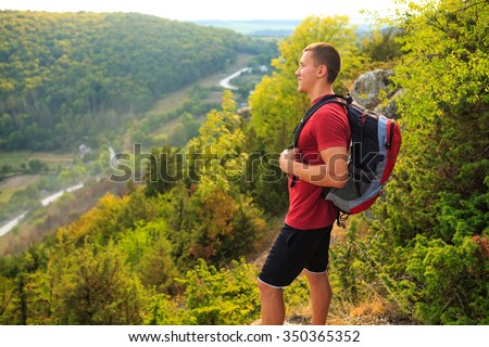 Hiking man portrait with backpack walking in nature. Caucasian man smiling happy with forest and mountains in background