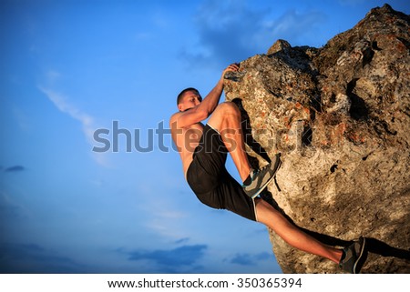 Muscular Climber climbs on a cliff with blue sky on background