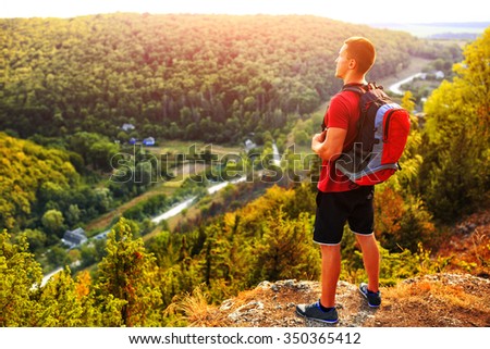 Hiking man portrait with backpack walking in nature. Caucasian man smiling happy with forest and mountains in background