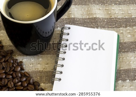 blank white page of notebook, some coffee beans and a black mug filled with coffee