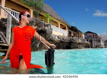 Beautiful woman in orange dress near a luxury villa on the ocean coastline