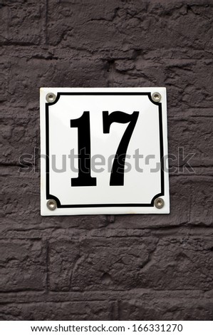House number seventeen on a white iron plate that is attached to a brown, stone wall