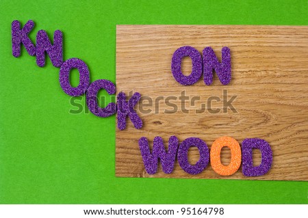 Superstition: The words KNOCK ON WOOD in glittering, purple, plastic characters on green paper and on paper with a wood structure