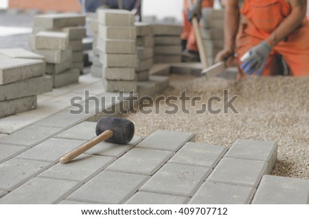 Rubber hammer for paving paths with workers and concrete tiles in background