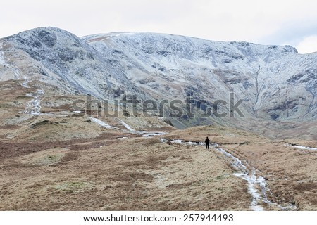 Man and dog climb a mountain in the snow in the Lake District, U
