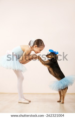 Little ballerina dancing with her cute dog in dance studio. They both wearing a tutu