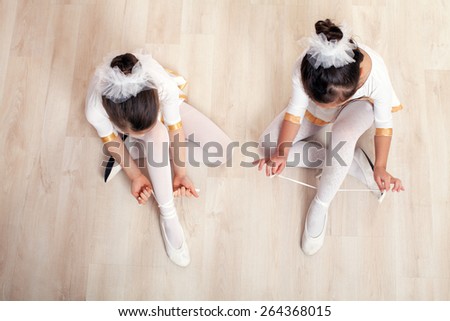 Two little ballerinas sitting on the floor and adjusting their ballet slippers. They are very cute