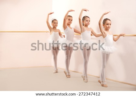 Group of four little ballerinas standing in row and practicing ballet and using stick on the wall. They are good friend and amazing dance performers