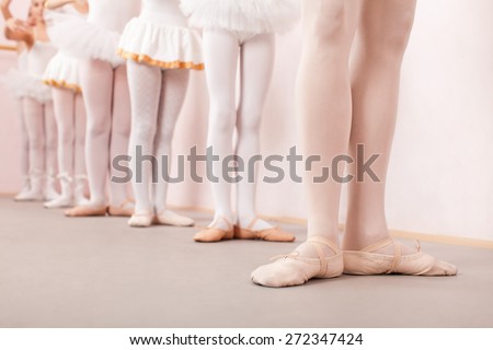 Group of six little ballerinas standing in row behind their ballet teacher and practicing ballet. They are all good friend and amazing dance performers