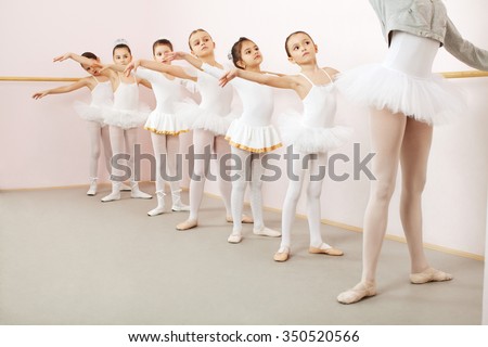 Little ballerinas dancing with ballet teacher in dance studio. Teacher doing exercise, and little ballerinas is watching and following her movements while using stick on the wall