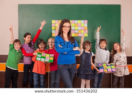 Children in elementary school posing with their teacher in front of chalkboard