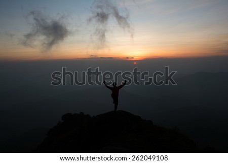 man stand on one leg  raise your hand and look sunset and fog on mountain