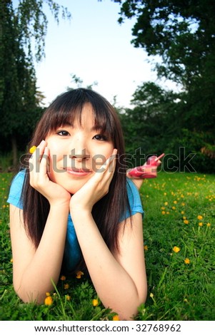 A girl laying in the grass holding a flower and smiling