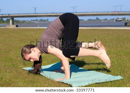 A woman doing bird stand yoga pose on both hands beside a riverbank