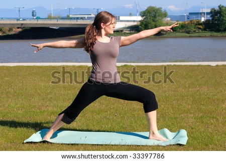 A woman doing a yoga warrior pose on a green space outside the city