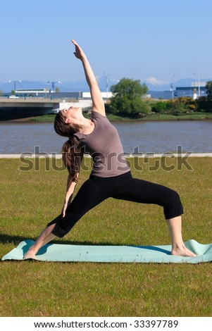 A woman doing a warrior yoga pose in a green space by the city