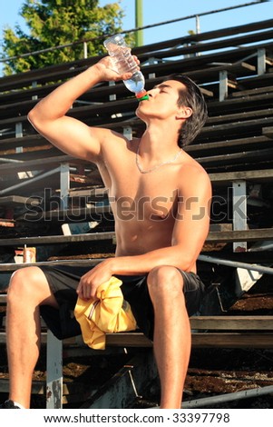 An attractive male athlete sitting on bleachers drinking a bottle of water