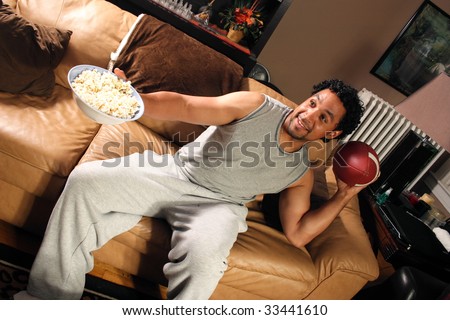 A man sitting on his couch with a bowl of popcorn set up to throw a football