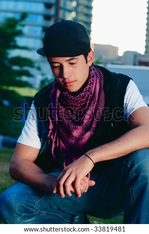 A hip hop boy crouching down looking at the ground in an urban park