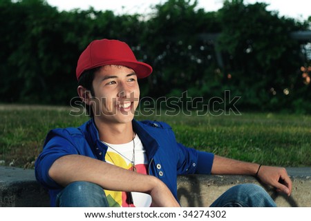 Man sitting in park wearing red ball cap and blue jacket smiling
