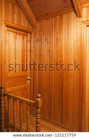Wooden house interior with two walls, sloping ceiling, a door and wooden railing