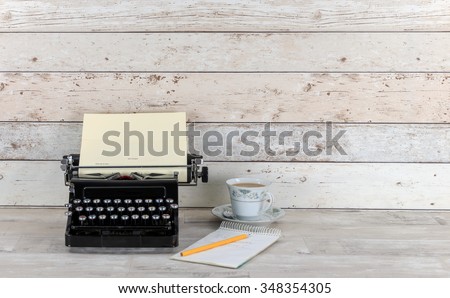 Old Technology, typewriter with notepad, pencil and cup of tea on an old shabby wood effect desk and background