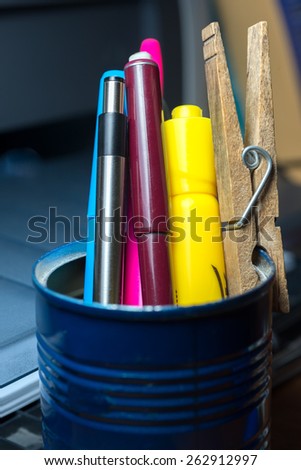 Close up of blue tin pencil cup containing pen, pencil, markers and wooden clothes pin.