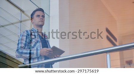 Image of an ambitious young man looking out at the view from his penthouse suit, while using his tablet to do research for investments