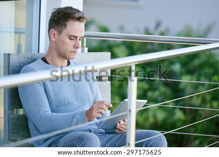 Image of a white young man sitting on his patio while looking up the weather on his tablet