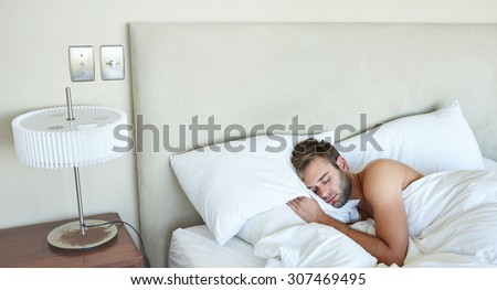 Young male sleeping alone in his luxurious white bedding on the morning of his business launch