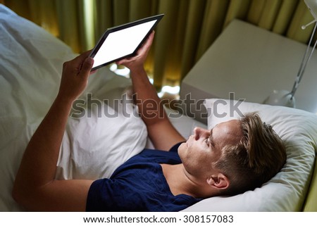 Handsome young businessman lying in bed checking in on his family on the other side of the world by using his tablet to video chat with them