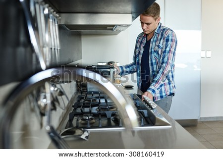 Handsome young entrepreneur making coffee in his modern kitchen using his coffee machine to make his morning espresso
