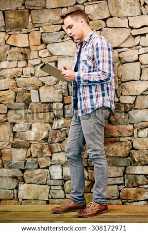 Young manager standing in front of a stone wall while reading an online journal on his tablet