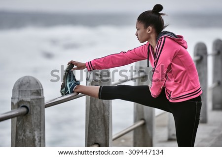 Close up image of an adult girl busy stretching her leg before going on a run nice and early in the morning, while she wears a pink jacket to keep her warm in the cold