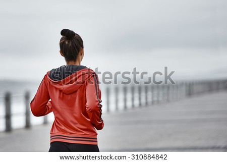 An image of a young mixed race females active life style as she takes her morning run along the sea side  while wearing a red jacket with lots of copy space