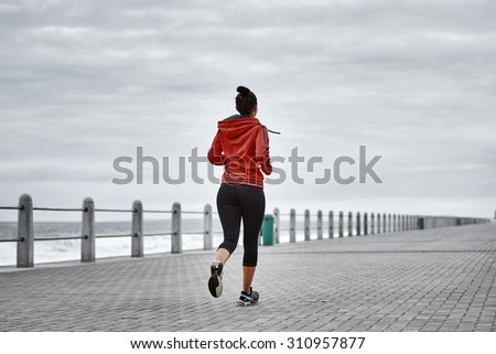 Active adult woman busy taking a morning run on the promenade along the ocean side with a dramatic sky