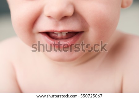 Cropped image of a baby\'s mouth open showing his first teeth, nose and his upper body, but not showing his eyes.