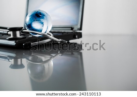 Glass globe and stethoscope on a computer keyboard.blue toned images.
