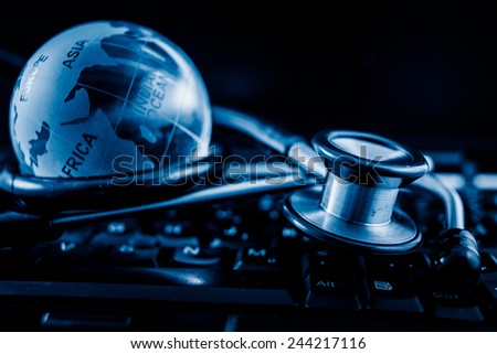 Glass globe and stethoscope on a computer keyboard.blue toned images.