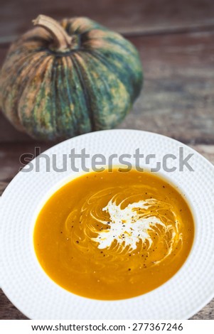 A bowl of asian style pumpkin soup with coconut milk on wooden background, warm tone. Soft focus on the soup and pumpkin on the blured background.